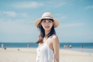 woman wearing hat stands beach front ocean