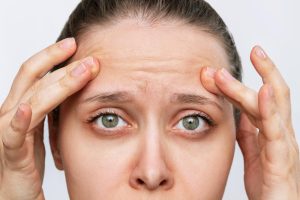 young caucasian worried woman touching forehead demonstrating wrinkles her face