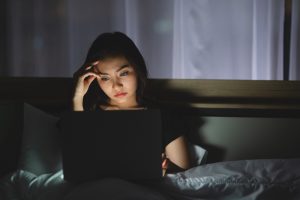 exhausted young business woman using laptop working late night bed