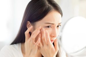 young woman looking mirror checking acne problem home