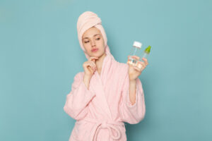 young female pink bathrobe after shower holding make up cleaner blue