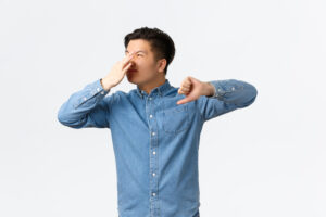 disgusted asian man looking away shut nose with fingers showing thumbs down complaining awful reek something stink bothered with bad smell standing white background