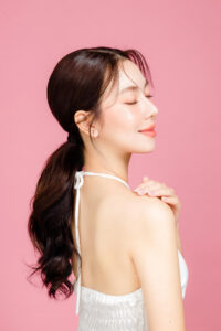 young asian woman gathered ponytail with natural makeup face have plump lips clean fresh skin wearing white camisole isolated pink background portrait cute female model studio